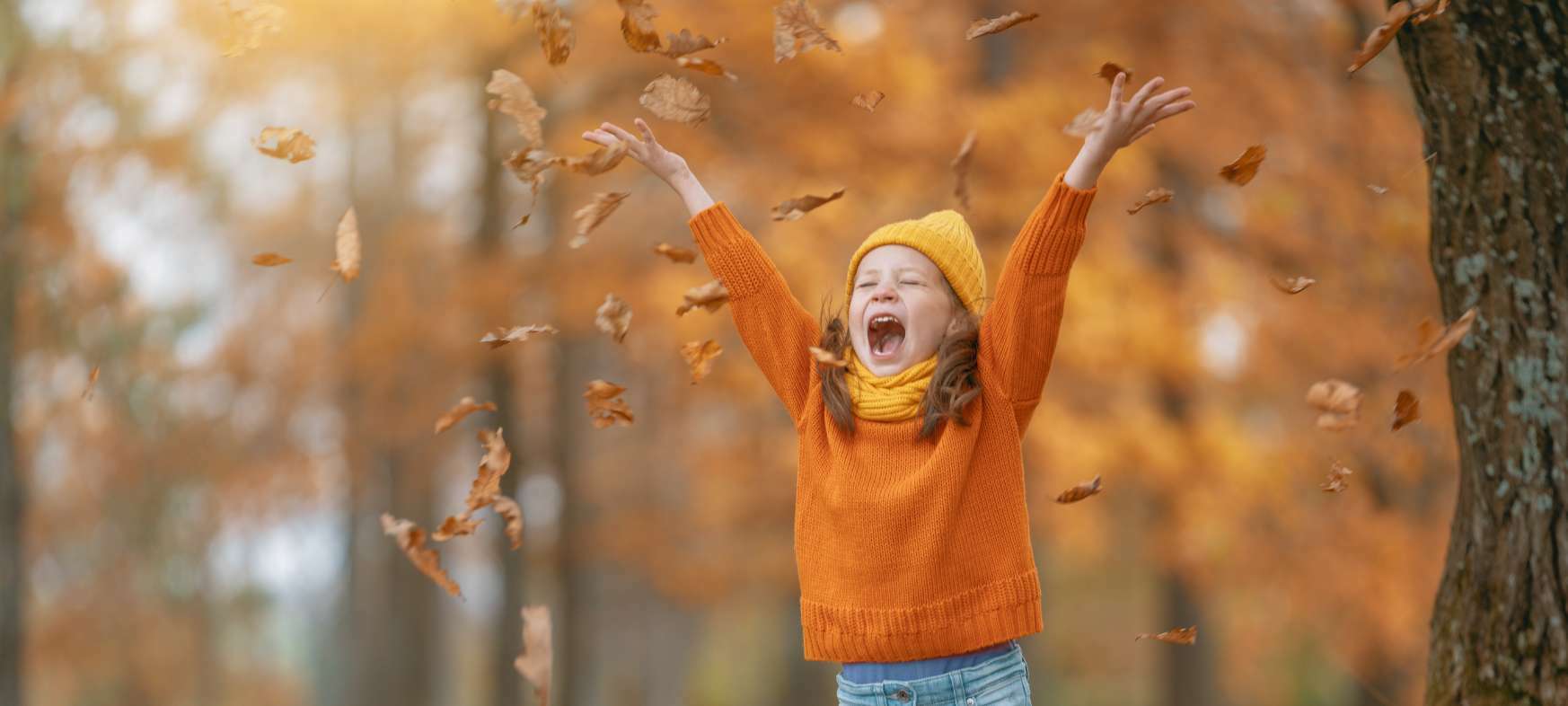 Kind spielt im Laub bei Herbstwetter