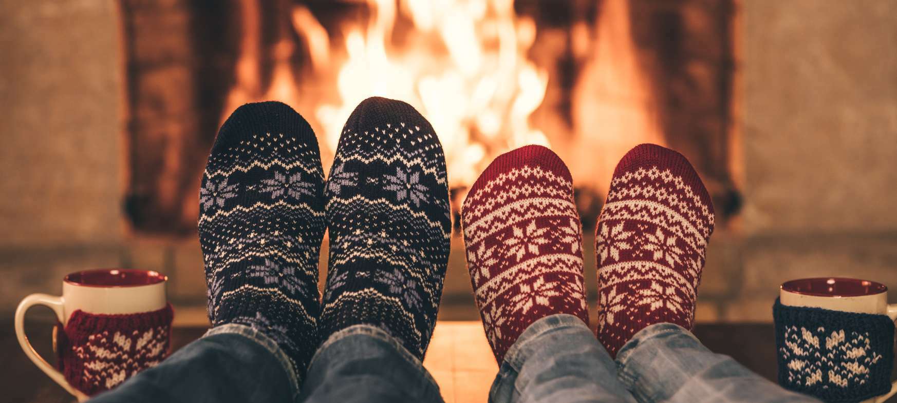 Zwei paar Füße mit Wintersocken vor dem Kamin